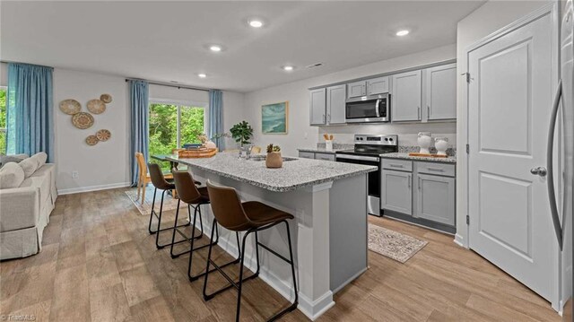 144 Rose Wind Way, Mayodan, NC 27027 - kitchen featuring an island with sink, light wood-type flooring, a kitchen bar, gray cabinets, and stainless steel appliances