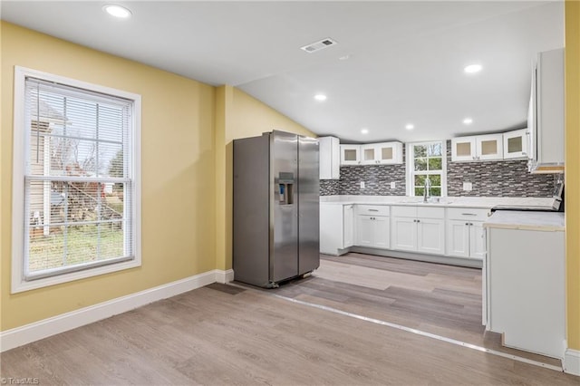 kitchen with lofted ceiling, white cabinets, decorative backsplash, light hardwood / wood-style floors, and stainless steel fridge with ice dispenser