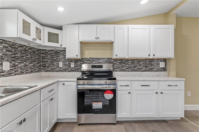 kitchen with tasteful backsplash, white cabinetry, stainless steel range, and lofted ceiling