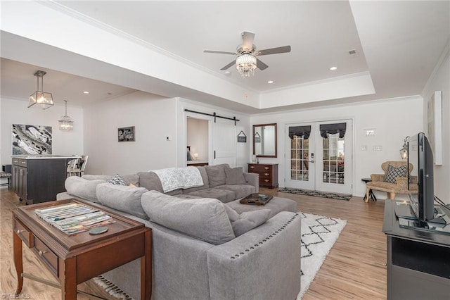 living room featuring ceiling fan, french doors, a raised ceiling, a barn door, and crown molding