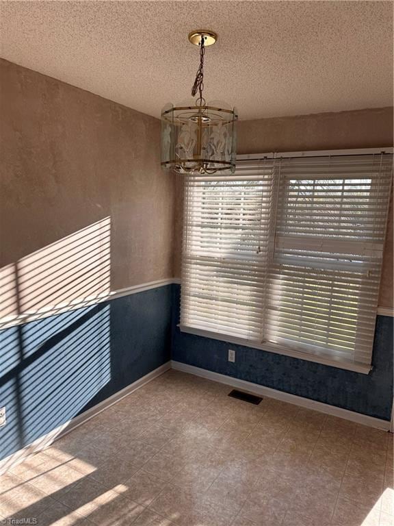 empty room with a textured ceiling and a notable chandelier