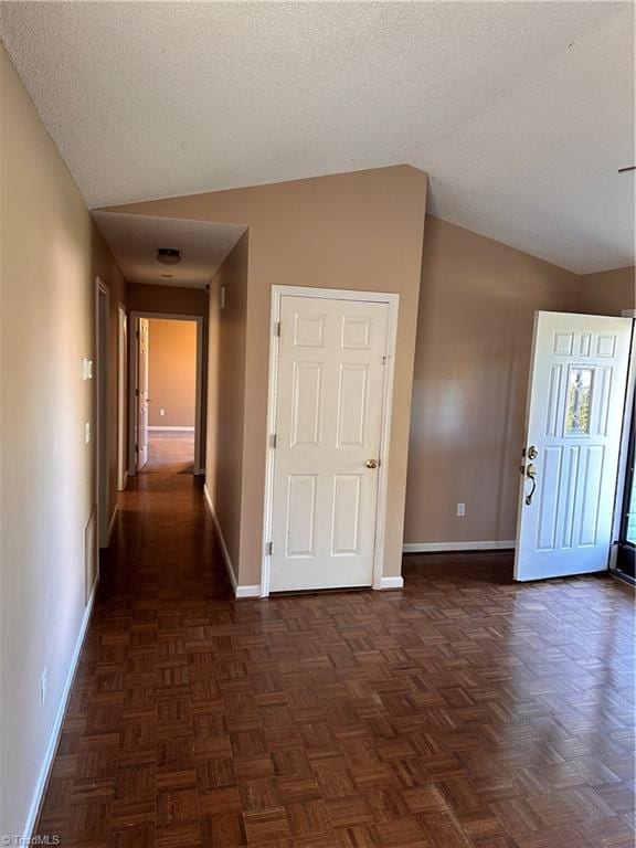 hall featuring a textured ceiling, dark parquet floors, and lofted ceiling