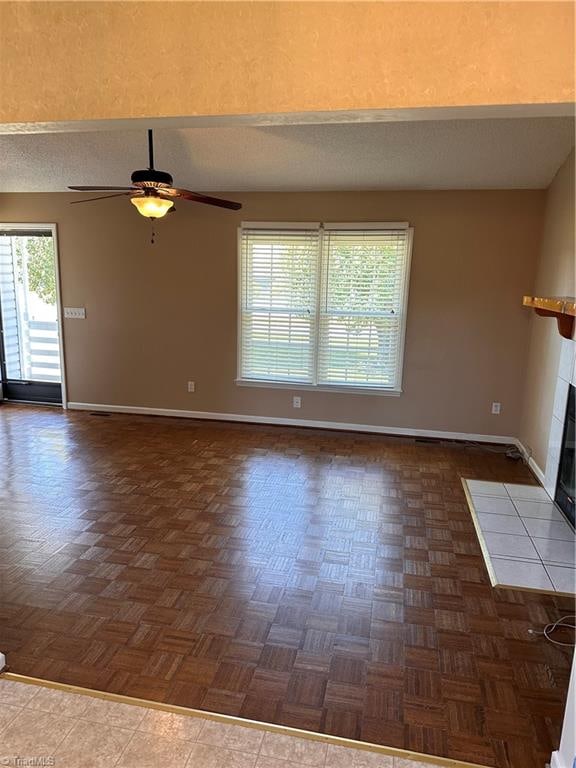 unfurnished living room with a tile fireplace, ceiling fan, and dark parquet flooring