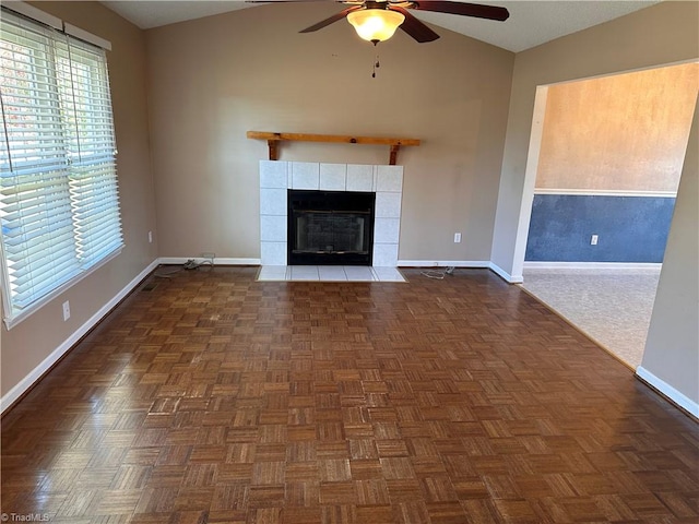 unfurnished living room featuring dark parquet floors, ceiling fan, lofted ceiling, and a tiled fireplace