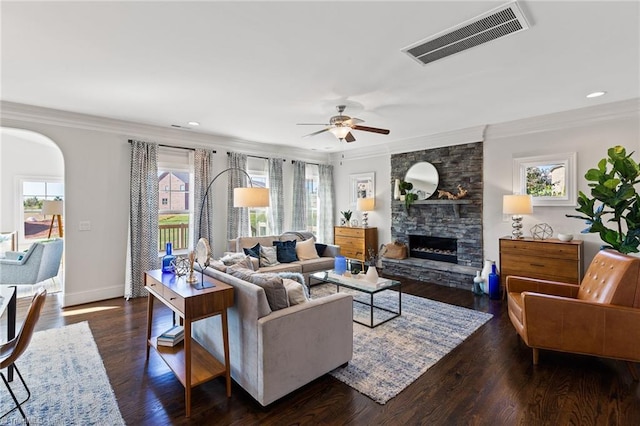 living room with a stone fireplace, crown molding, ceiling fan, and a healthy amount of sunlight