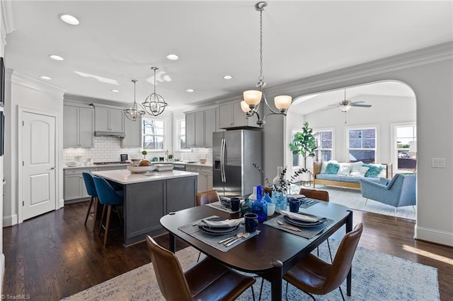 dining space featuring dark wood-type flooring, ceiling fan with notable chandelier, and ornamental molding