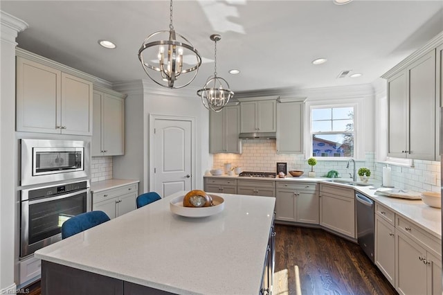 kitchen featuring a center island, sink, hanging light fixtures, dark wood-type flooring, and stainless steel appliances