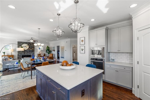 kitchen featuring dark hardwood / wood-style flooring, backsplash, ceiling fan with notable chandelier, stainless steel appliances, and a fireplace