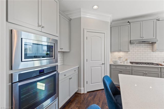 kitchen featuring dark hardwood / wood-style flooring, tasteful backsplash, gray cabinetry, stainless steel appliances, and crown molding