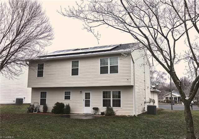 back of house featuring solar panels, cooling unit, and a lawn