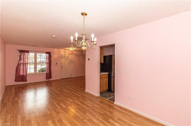 unfurnished room featuring light wood-type flooring, a textured ceiling, and an inviting chandelier