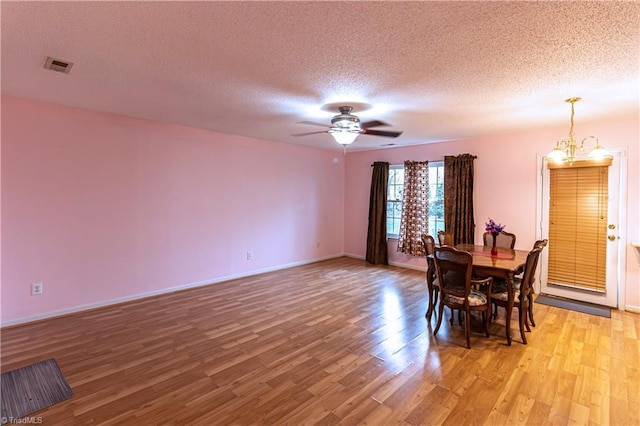 dining space featuring ceiling fan with notable chandelier, a textured ceiling, and light wood-type flooring