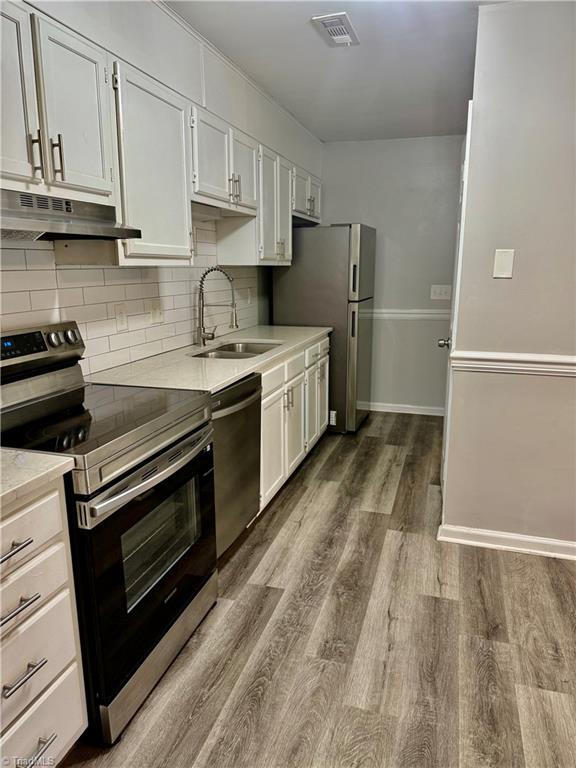kitchen featuring appliances with stainless steel finishes, under cabinet range hood, a sink, decorative backsplash, and dark wood-style floors