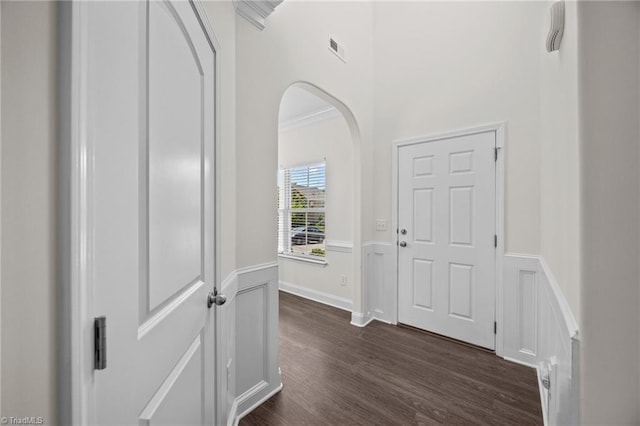 corridor with a wainscoted wall, arched walkways, dark wood-style flooring, and a decorative wall