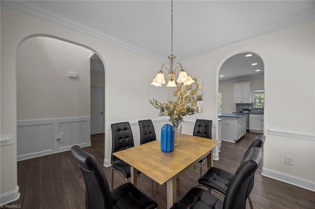 dining room featuring arched walkways, dark wood-style floors, a chandelier, crown molding, and a wainscoted wall
