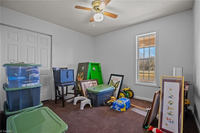 playroom featuring a textured ceiling, dark colored carpet, and ceiling fan