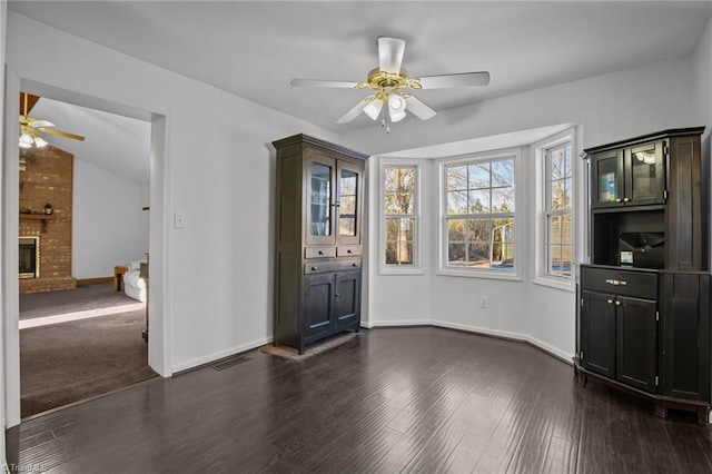 unfurnished dining area featuring a brick fireplace, dark hardwood / wood-style floors, lofted ceiling, and ceiling fan