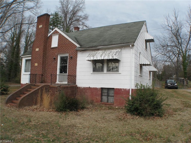 exterior space with a shingled roof, a yard, and a chimney