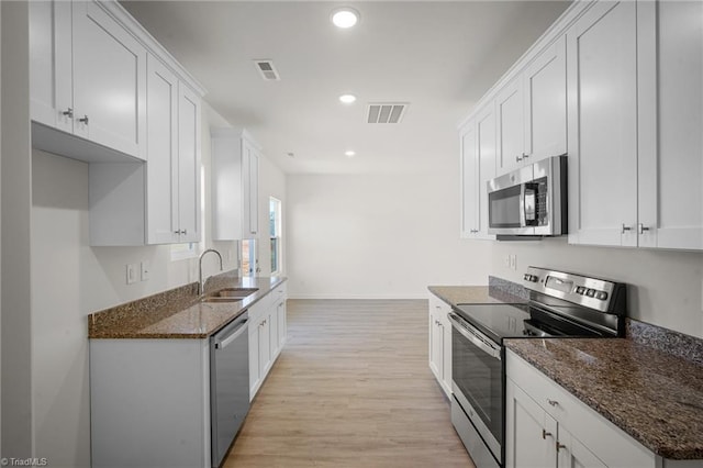 kitchen with stainless steel appliances, white cabinetry, sink, and dark stone counters