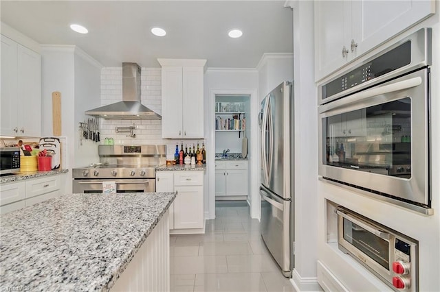 kitchen with stainless steel appliances, white cabinetry, and wall chimney range hood