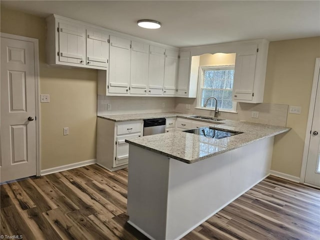 kitchen with dark wood-type flooring, a peninsula, light stone countertops, black electric cooktop, and a sink