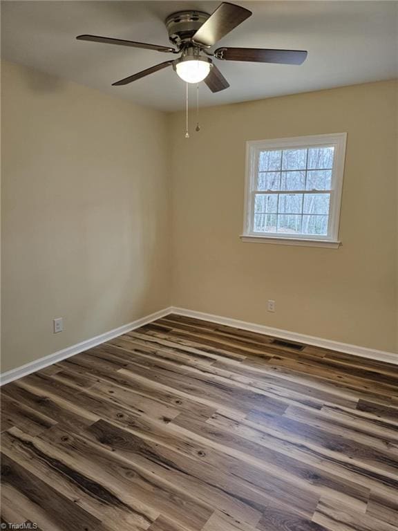 empty room featuring dark wood-style flooring, visible vents, and baseboards