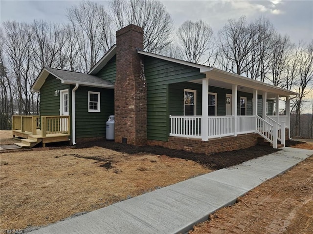 view of front of home featuring a porch, a chimney, and a shingled roof