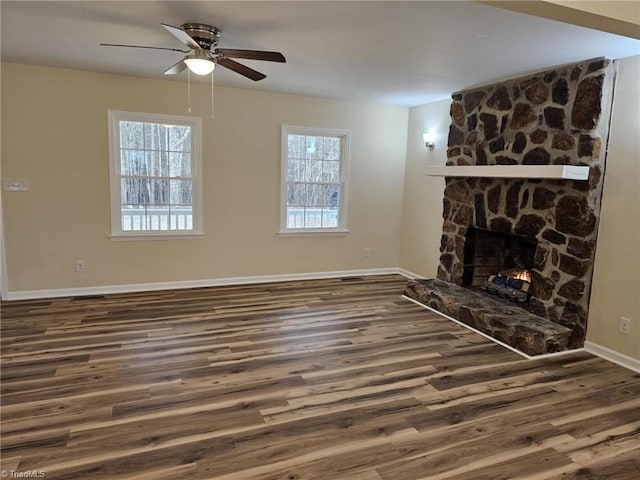 unfurnished living room with a stone fireplace, wood finished floors, a ceiling fan, and baseboards