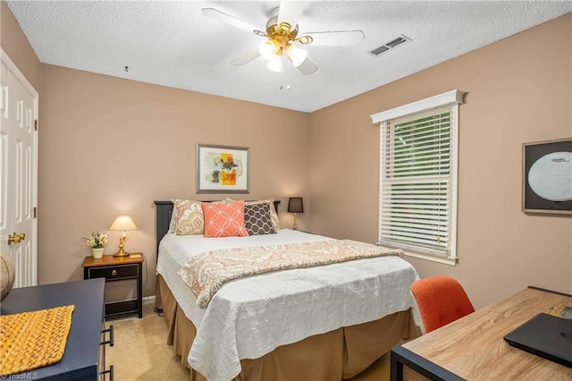 bedroom featuring visible vents, a textured ceiling, ceiling fan, and light colored carpet