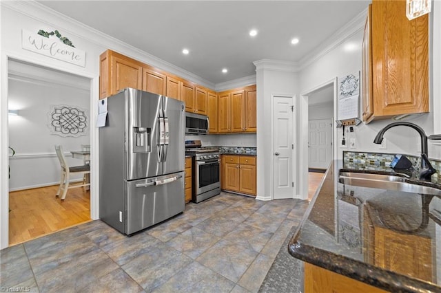 kitchen with appliances with stainless steel finishes, crown molding, a sink, and dark stone countertops