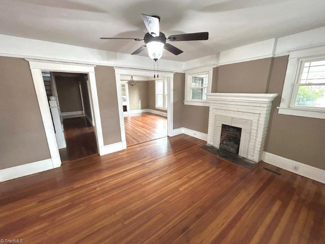 unfurnished living room with a brick fireplace, visible vents, baseboards, and wood finished floors