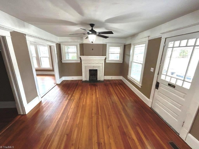 unfurnished living room featuring a brick fireplace, baseboards, visible vents, and dark wood-style flooring