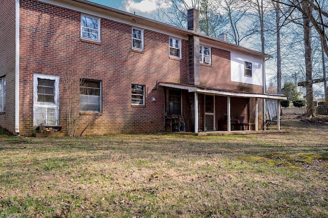 rear view of property with brick siding, a lawn, and a chimney