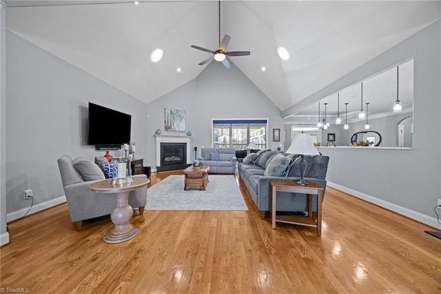 living room with wood finished floors, baseboards, high vaulted ceiling, ceiling fan, and a glass covered fireplace