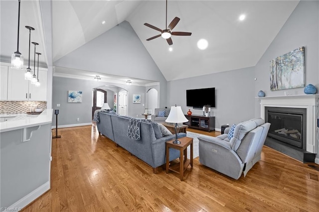 living area featuring baseboards, high vaulted ceiling, arched walkways, ceiling fan, and light wood-type flooring