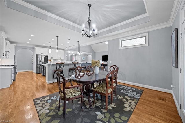 dining room with light wood finished floors, a chandelier, a tray ceiling, ornamental molding, and arched walkways