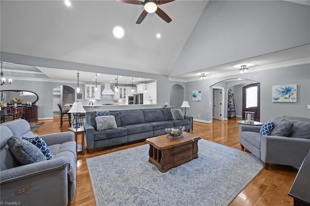 living area with baseboards, light wood finished floors, high vaulted ceiling, arched walkways, and ceiling fan