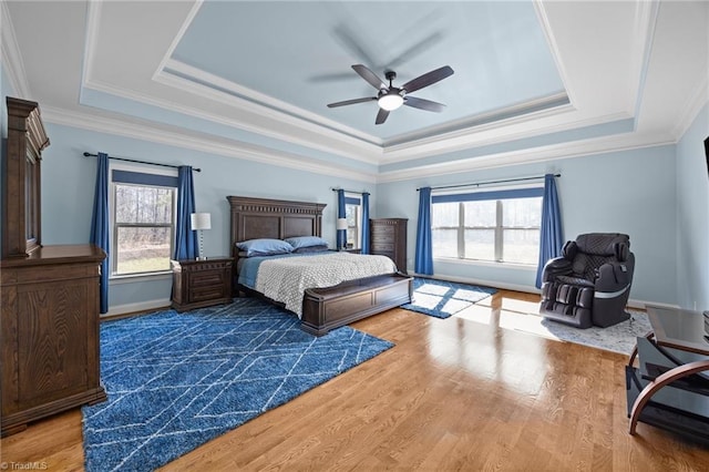 bedroom featuring a ceiling fan, wood finished floors, baseboards, ornamental molding, and a raised ceiling