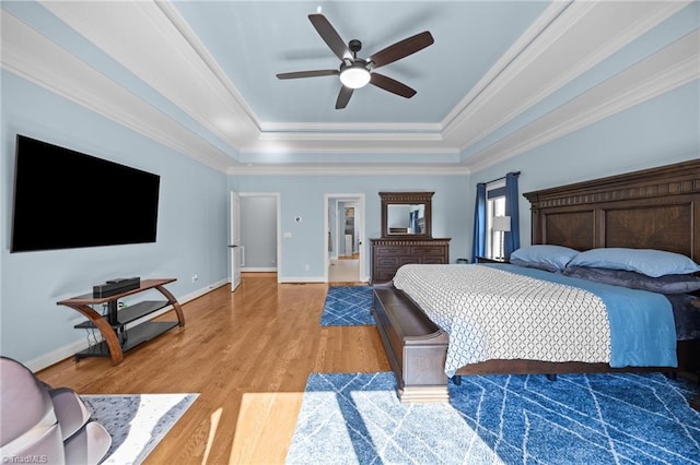 bedroom with baseboards, a raised ceiling, light wood-style flooring, and ornamental molding