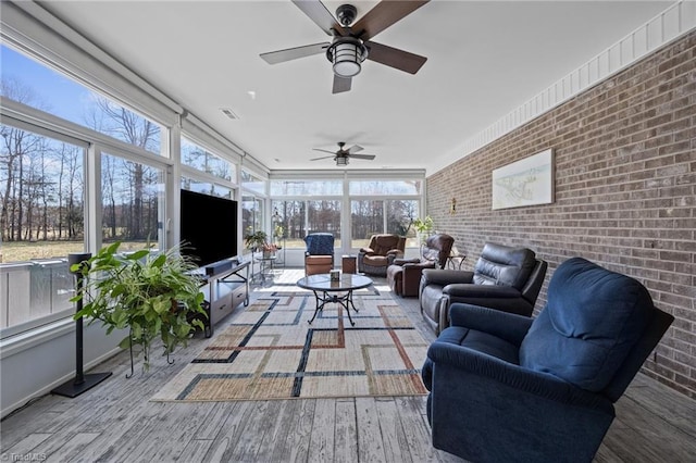 living area featuring a ceiling fan, wood finished floors, visible vents, and brick wall