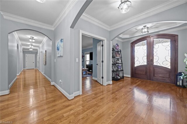 entrance foyer with light wood-type flooring, arched walkways, crown molding, and french doors