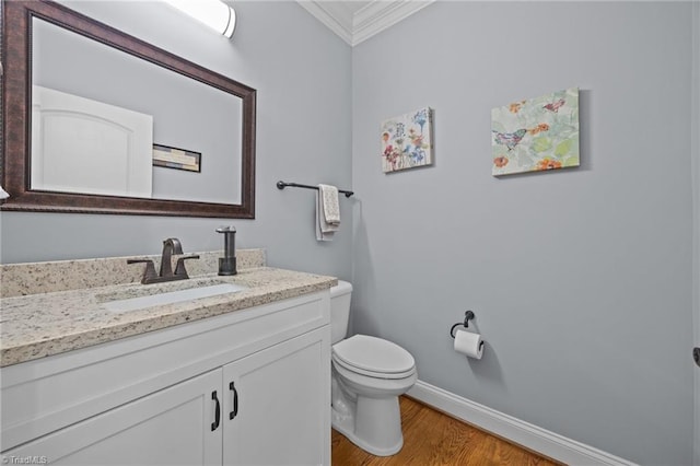 bathroom featuring baseboards, toilet, ornamental molding, wood finished floors, and vanity