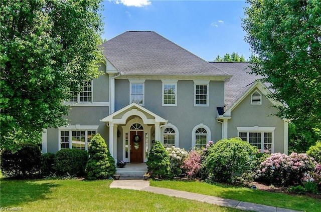 view of front of property featuring a shingled roof, a front lawn, and stucco siding