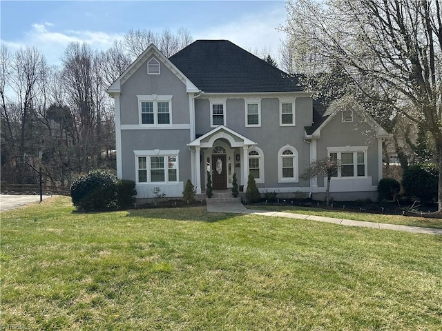 traditional home with a shingled roof, a front lawn, and stucco siding