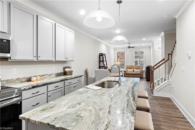 kitchen featuring stainless steel electric stove, a sink, dark wood-style flooring, a ceiling fan, and a breakfast bar area