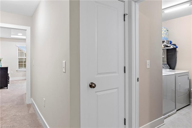 hall featuring washing machine and clothes dryer, light carpet, and baseboards