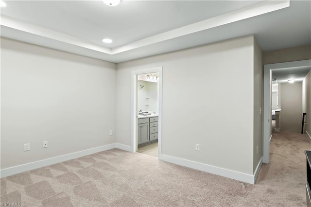 unfurnished bedroom featuring light carpet, a tray ceiling, baseboards, connected bathroom, and recessed lighting