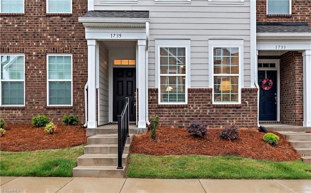 view of exterior entry featuring brick siding and a shingled roof