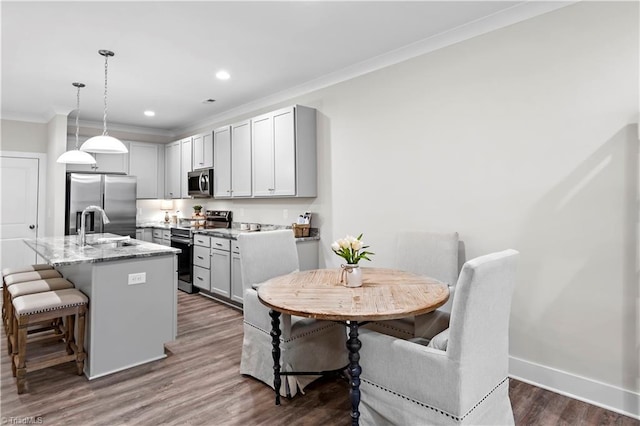 kitchen with appliances with stainless steel finishes, ornamental molding, a sink, a breakfast bar area, and dark wood-style floors