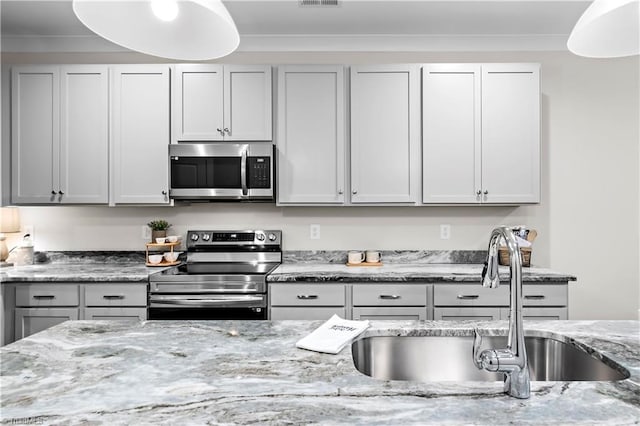 kitchen with appliances with stainless steel finishes, a sink, light stone countertops, and gray cabinetry